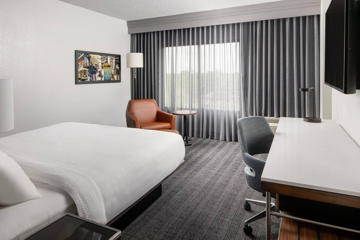 A hotel room with a large bed, a desk, a chair, a small table, a lamp, and a painting on the wall.