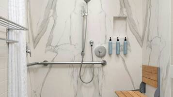 A modern shower with a marble wall, a grab bar, a handheld showerhead, and a shelf with toiletries.
