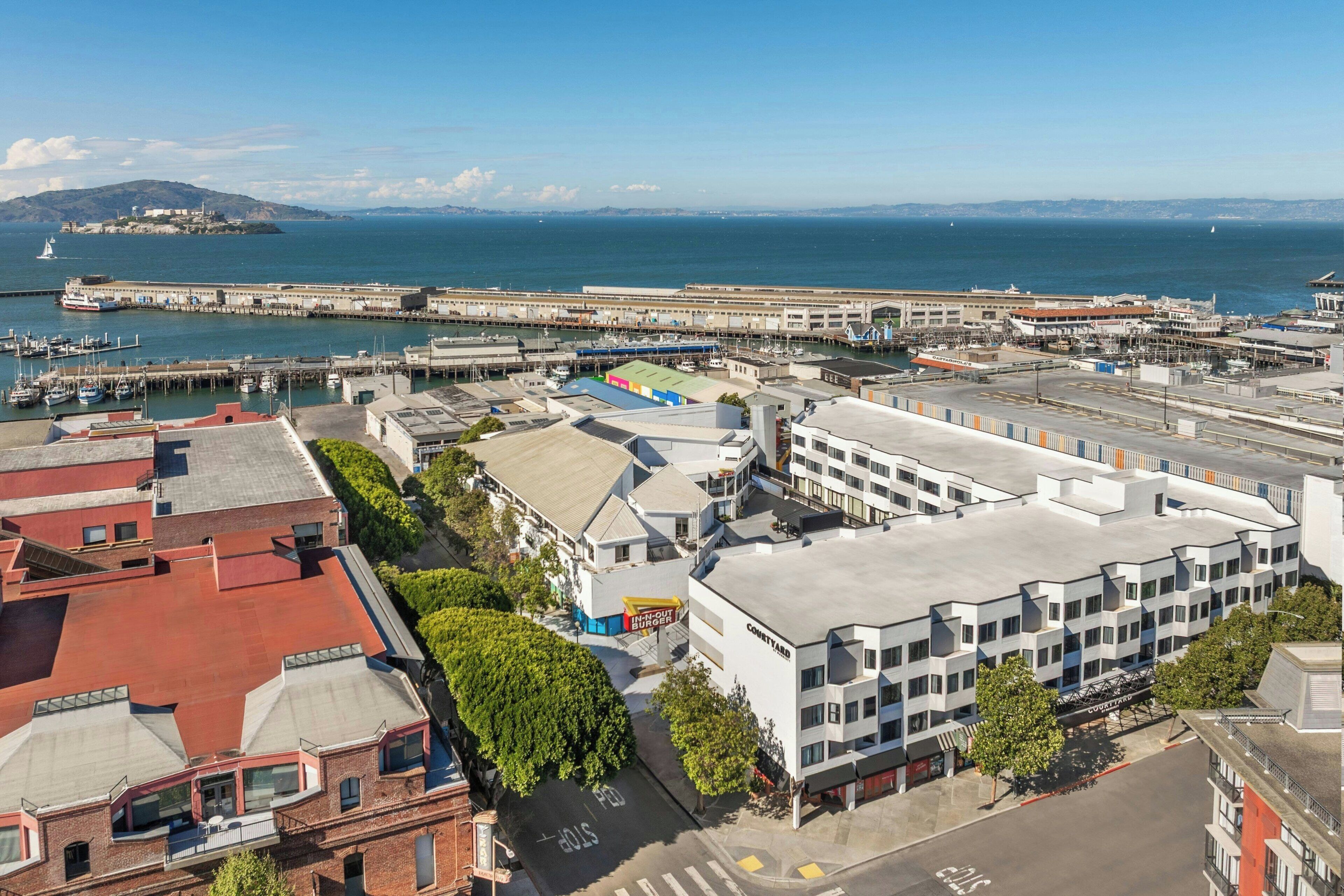 Vue aérienne d’une zone urbaine côtière, avec un port de plaisance, des bâtiments et une île au loin.