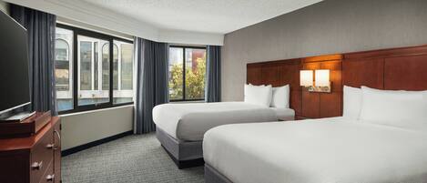 A hotel room with two beds, a TV, a dresser, and a window with curtains.