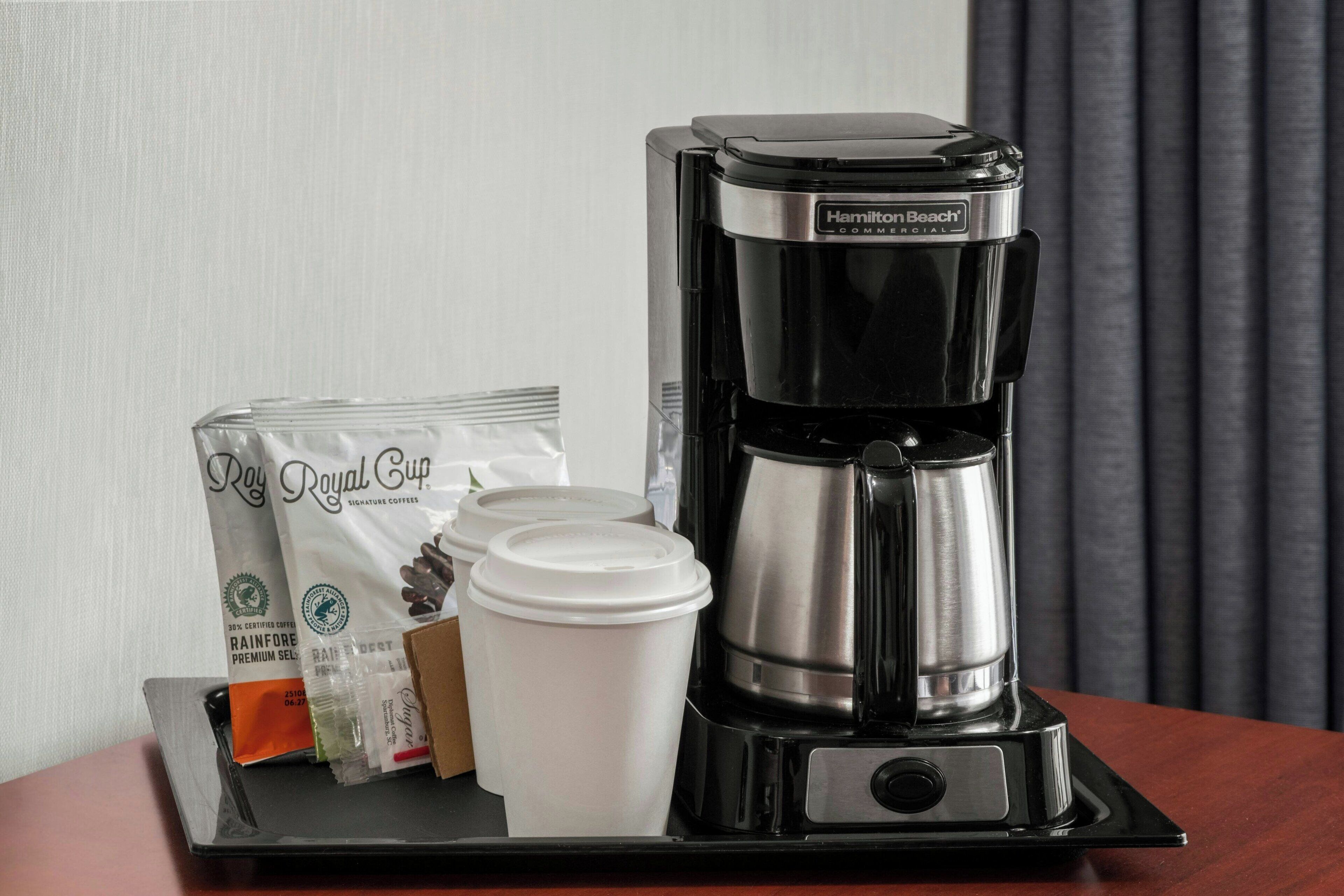 Una cafetera, cápsulas de café y vasos desechables sobre una bandeja.