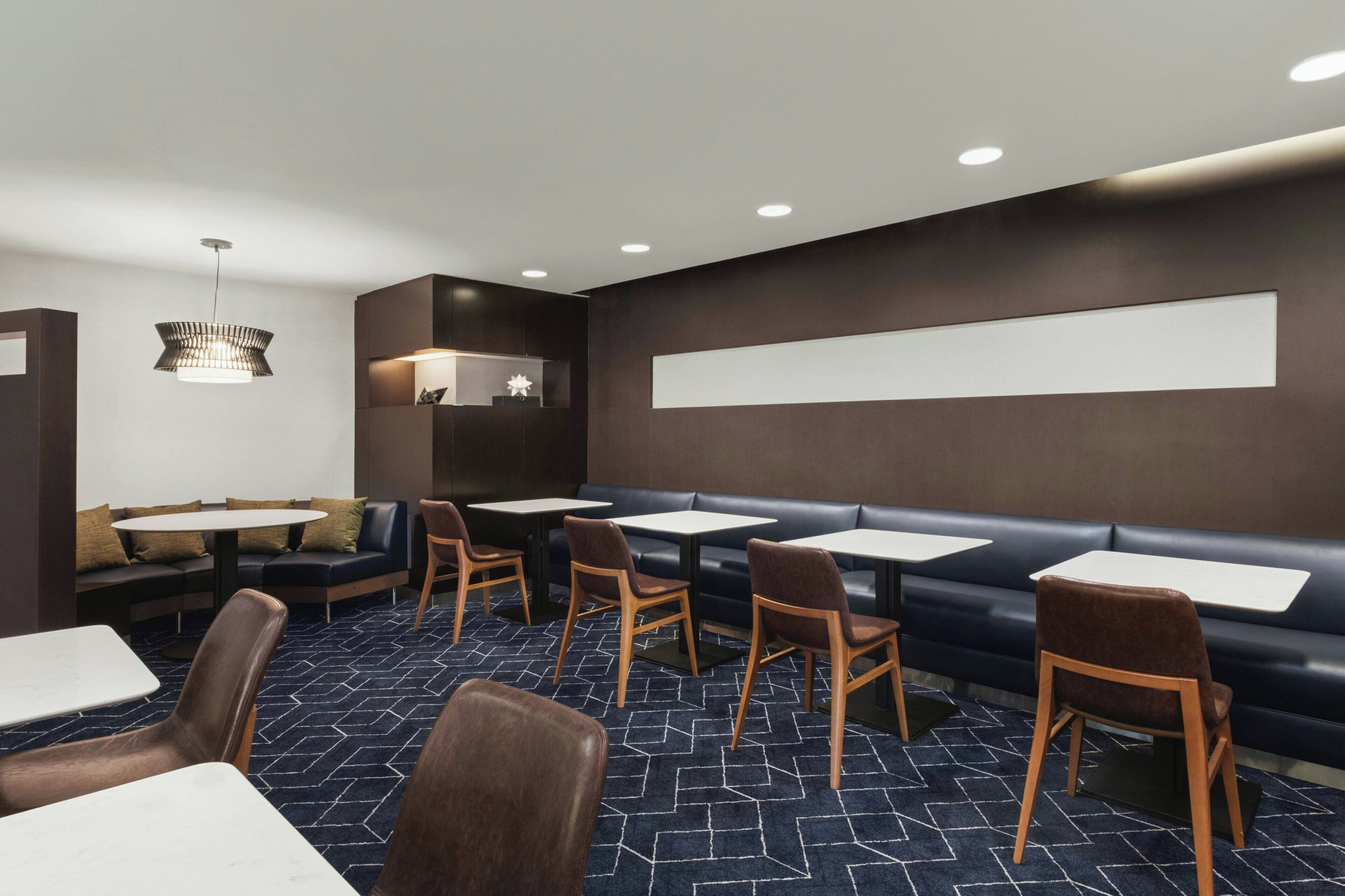 A modern restaurant with a dark color scheme, featuring a long counter, booths, and a patterned carpet.