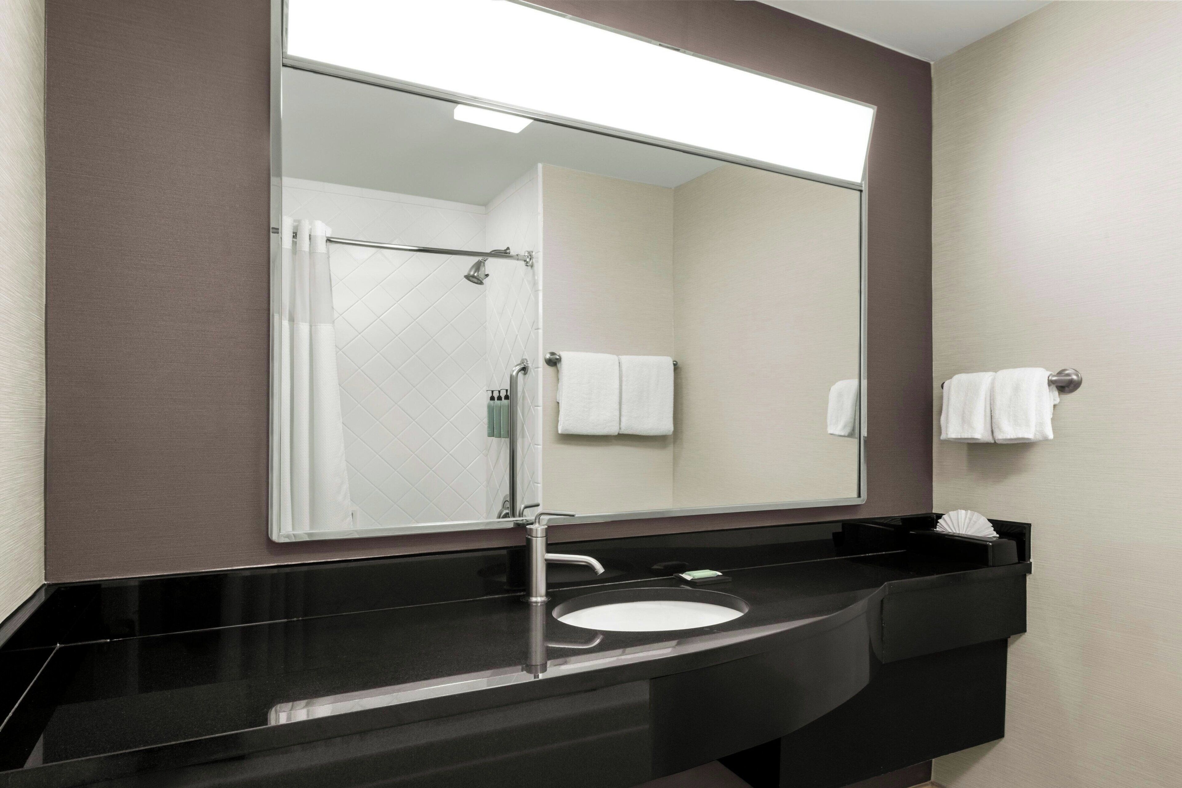 A modern bathroom with a black sink, a large mirror, and a shower visible in the reflection.