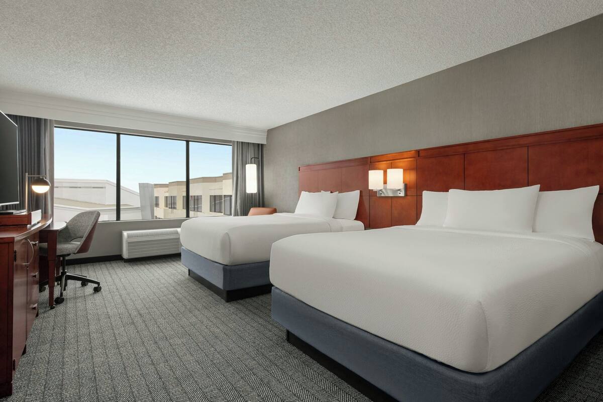 A hotel room with two beds, a desk, and a chair.