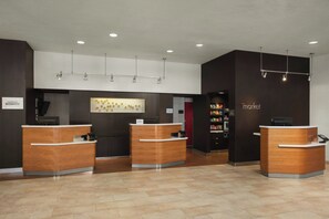 A hotel reception area with three wooden reception desks, a wall-mounted light fixture, and a 'Market' sign.