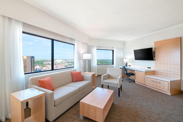 A hotel room with a sofa, armchair, desk, and television. - Delta Hotels by Marriott Regina (Regina)