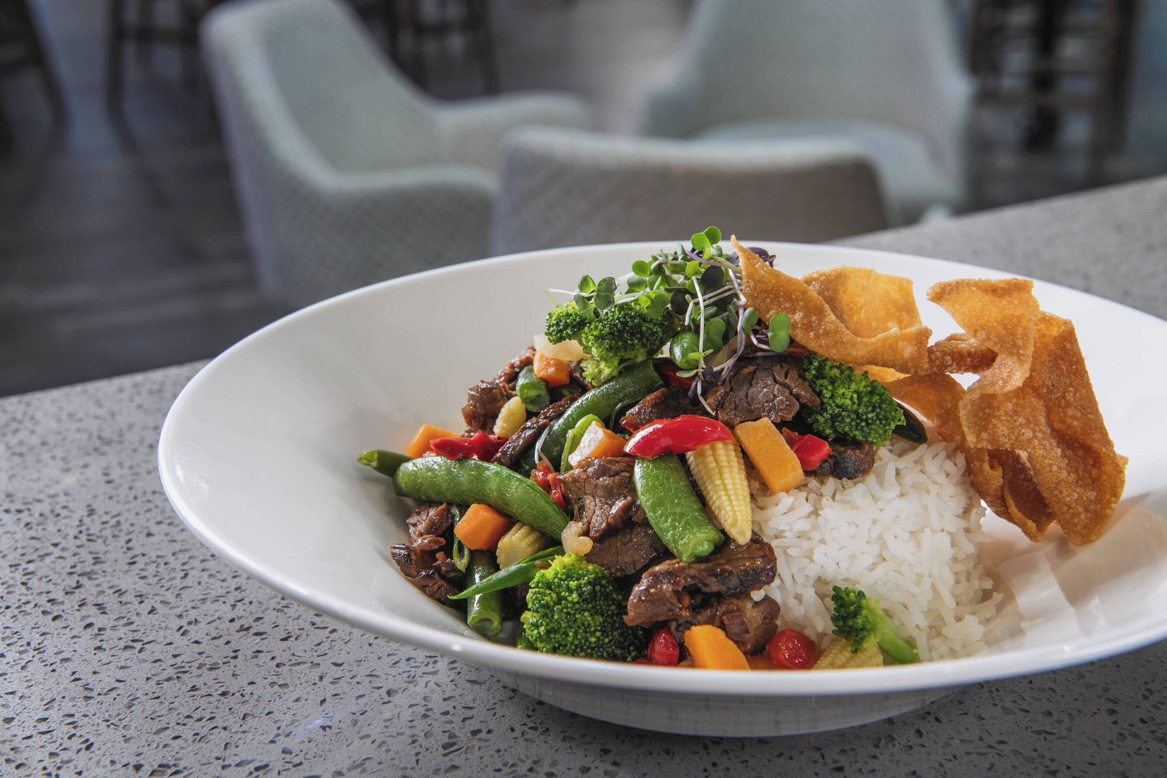 Un bol de arroz con salteado de carne y verduras, servido en un plato blanco.