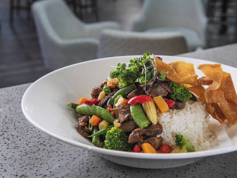 Un bol de arroz con salteado de carne y verduras, servido en un plato blanco.