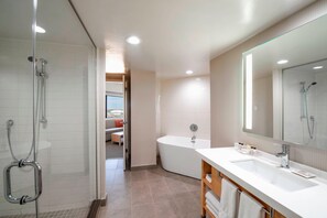 A modern bathroom with a glass-enclosed shower, a freestanding bathtub, and a large mirror above the sink. - Delta Hotels by Marriott Regina (Regina)
