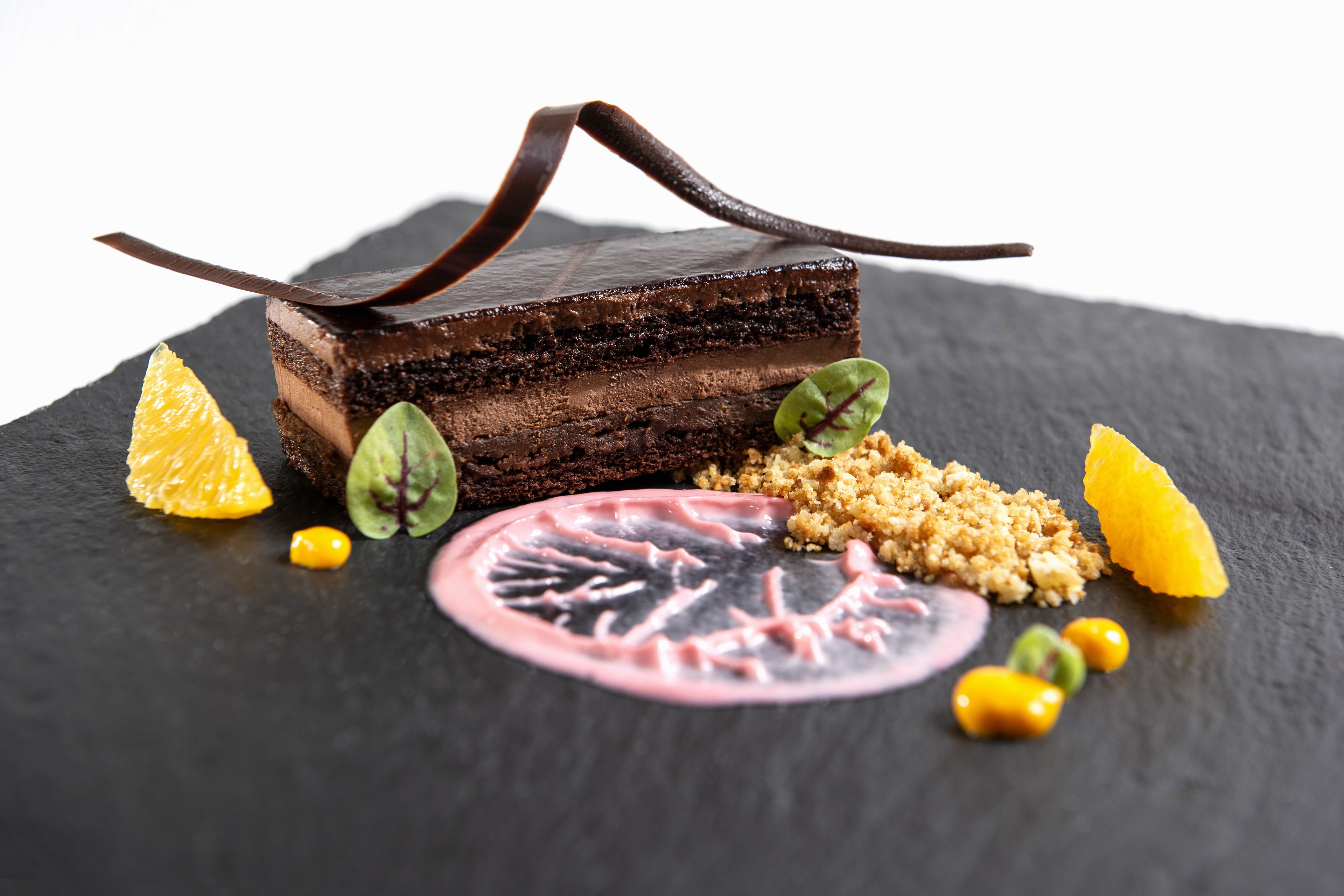 A dessert with chocolate layers, garnished with orange slices and green leaves on a dark slate plate.