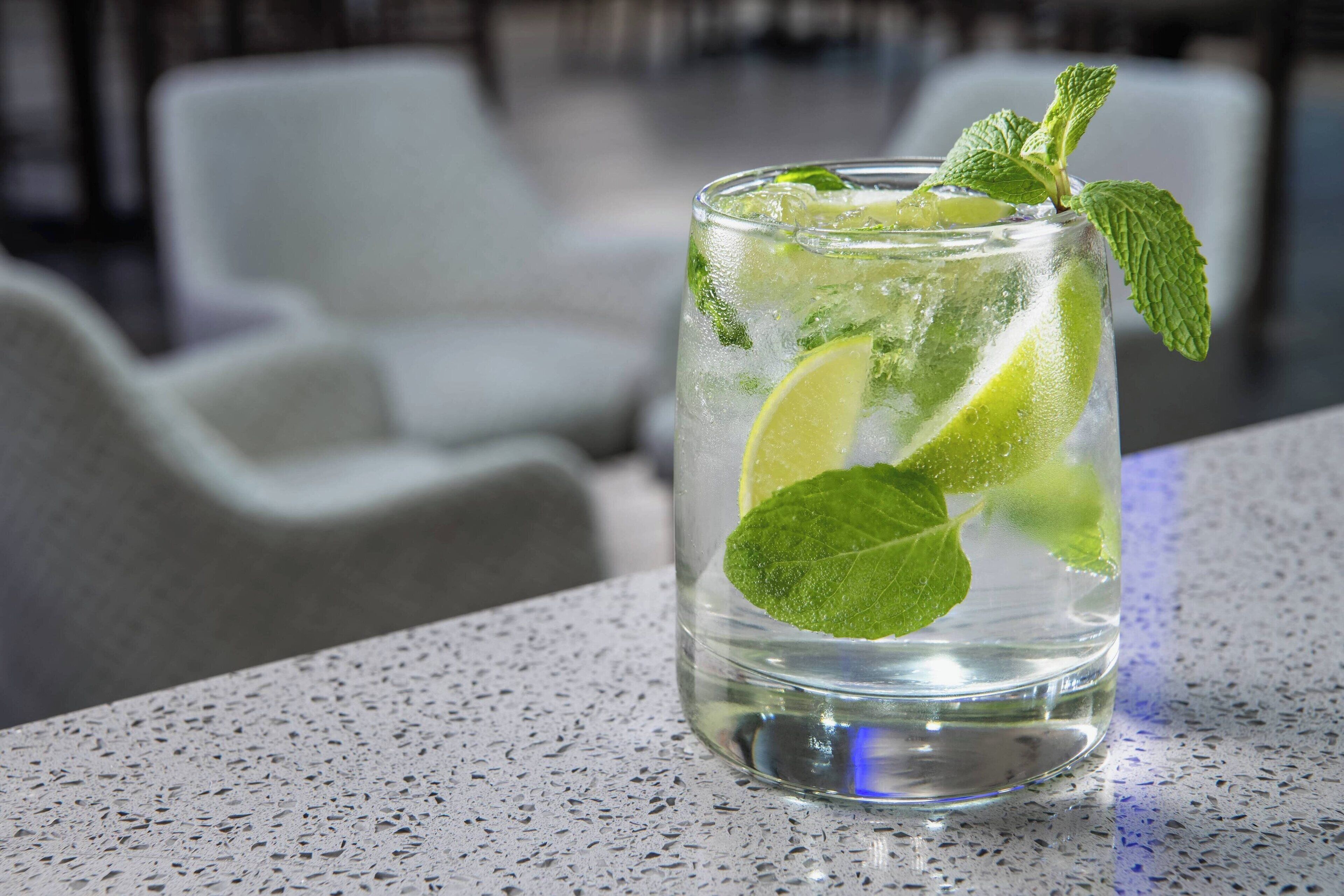Un vaso transparente con hielo, lima y hojas de menta sobre una encimera con motas.