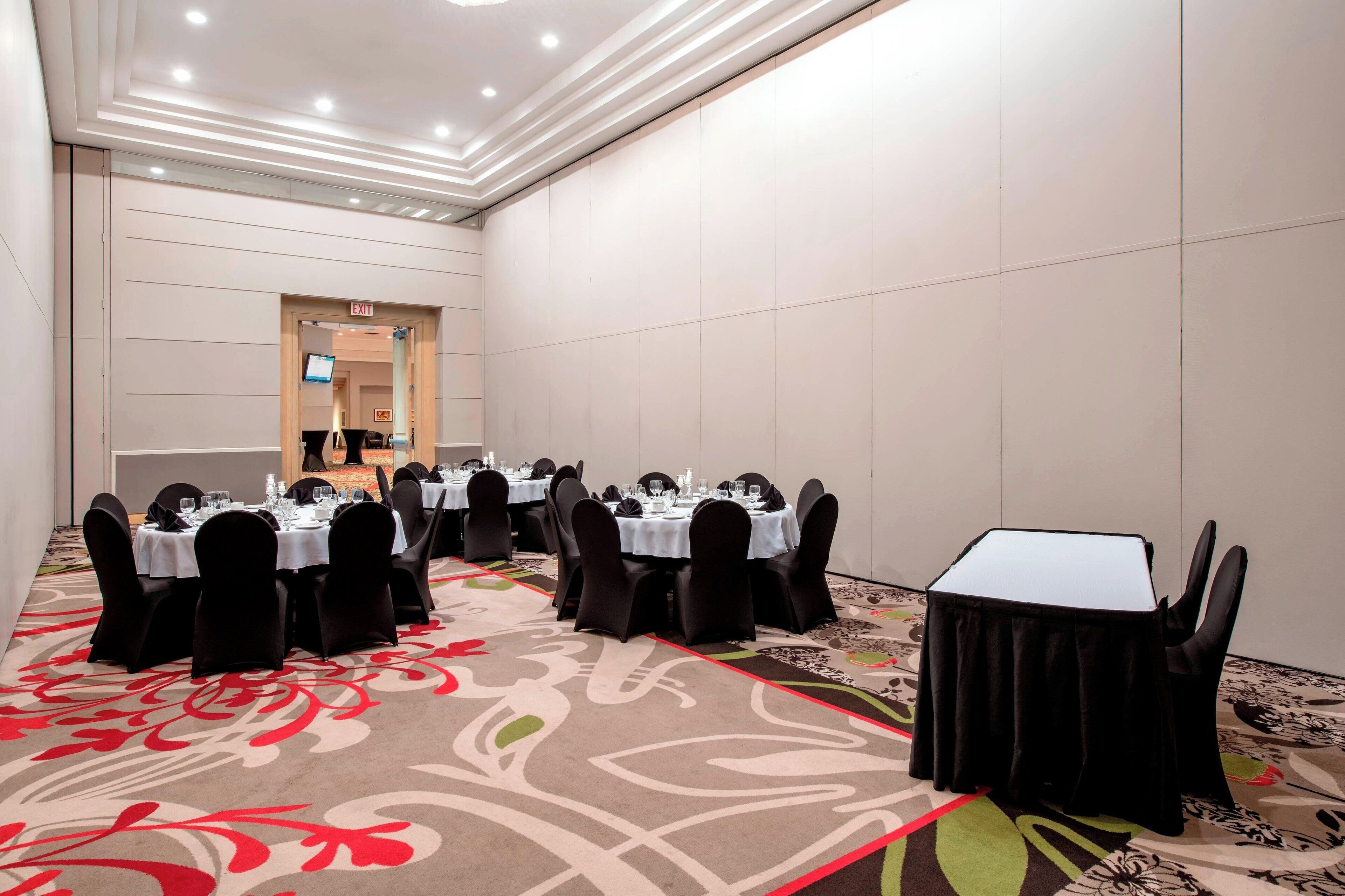 A conference room with round tables, black chairs, and a carpeted floor.