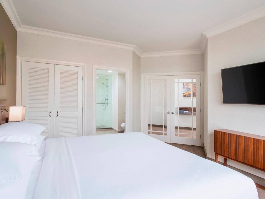 A hotel room with a large bed, a TV mounted on the wall, a wooden cabinet, and a bathroom visible through an open door.