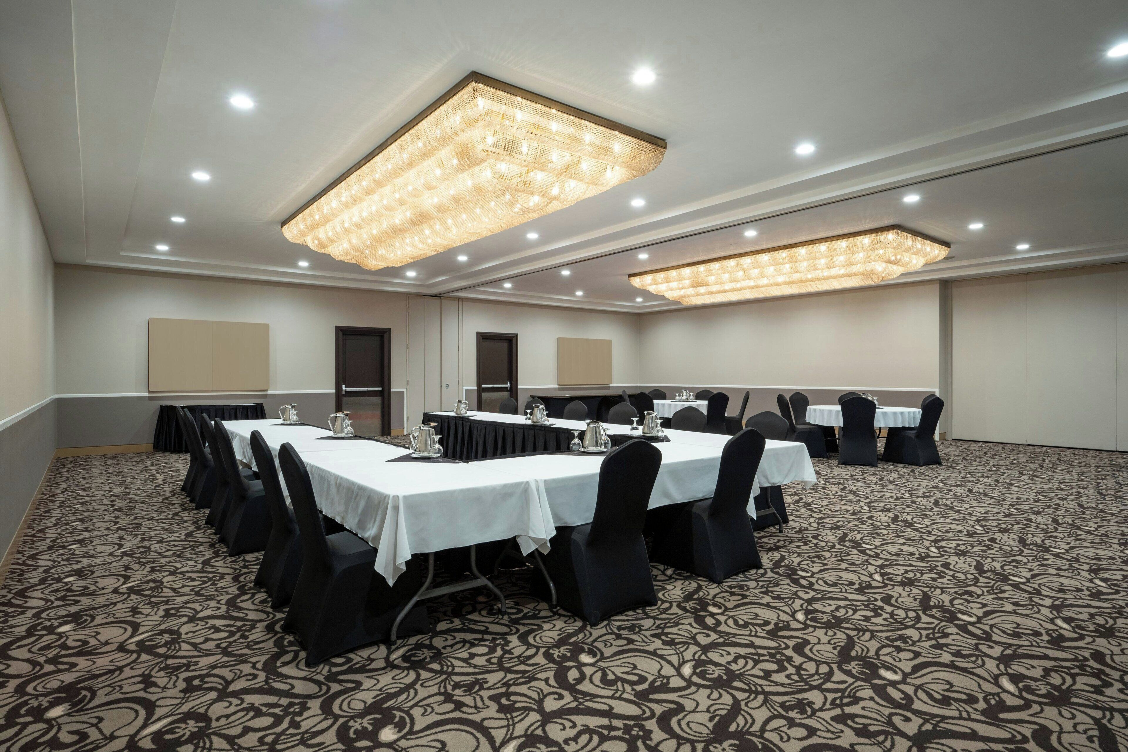 A conference room with multiple tables and chairs, equipped with overhead lighting and a patterned carpet.