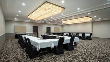 A conference room with multiple tables and chairs, equipped with overhead lighting and a patterned carpet.