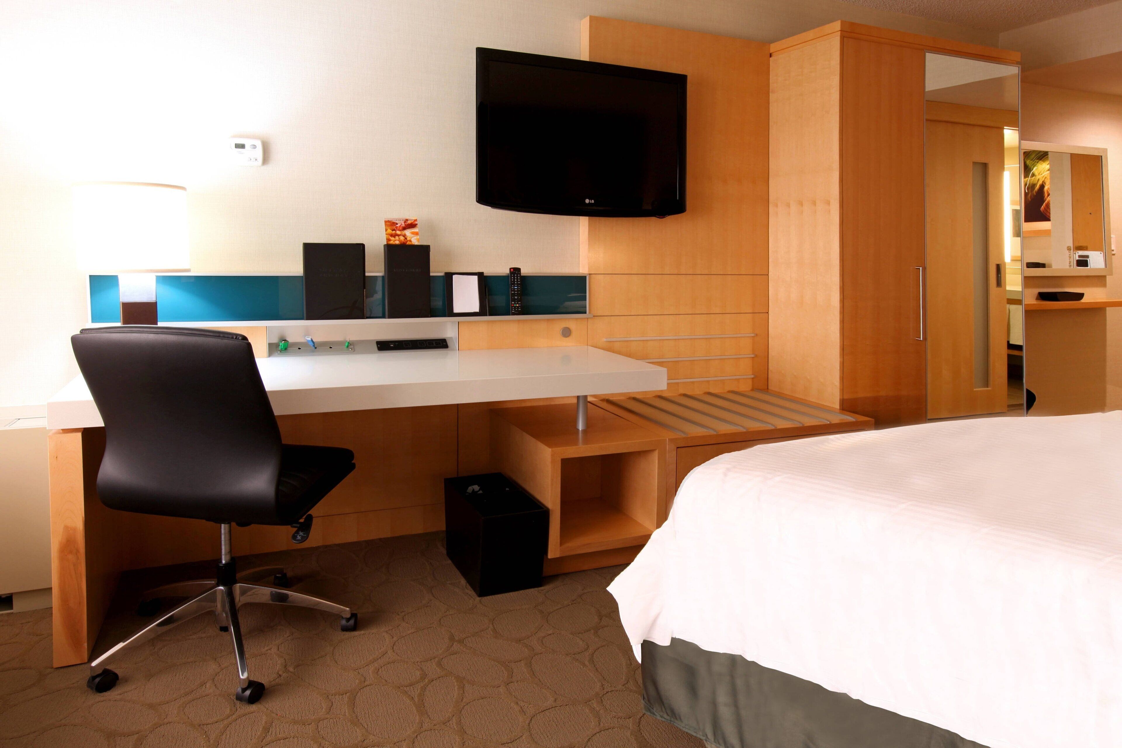 A hotel room with a bed, a desk with a chair, a television, and a wardrobe.