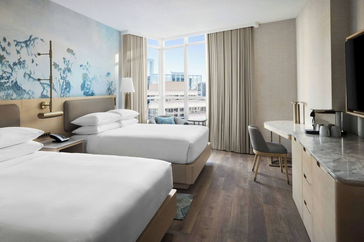 A hotel room with two beds, a desk, a chair, a TV, and a city view.