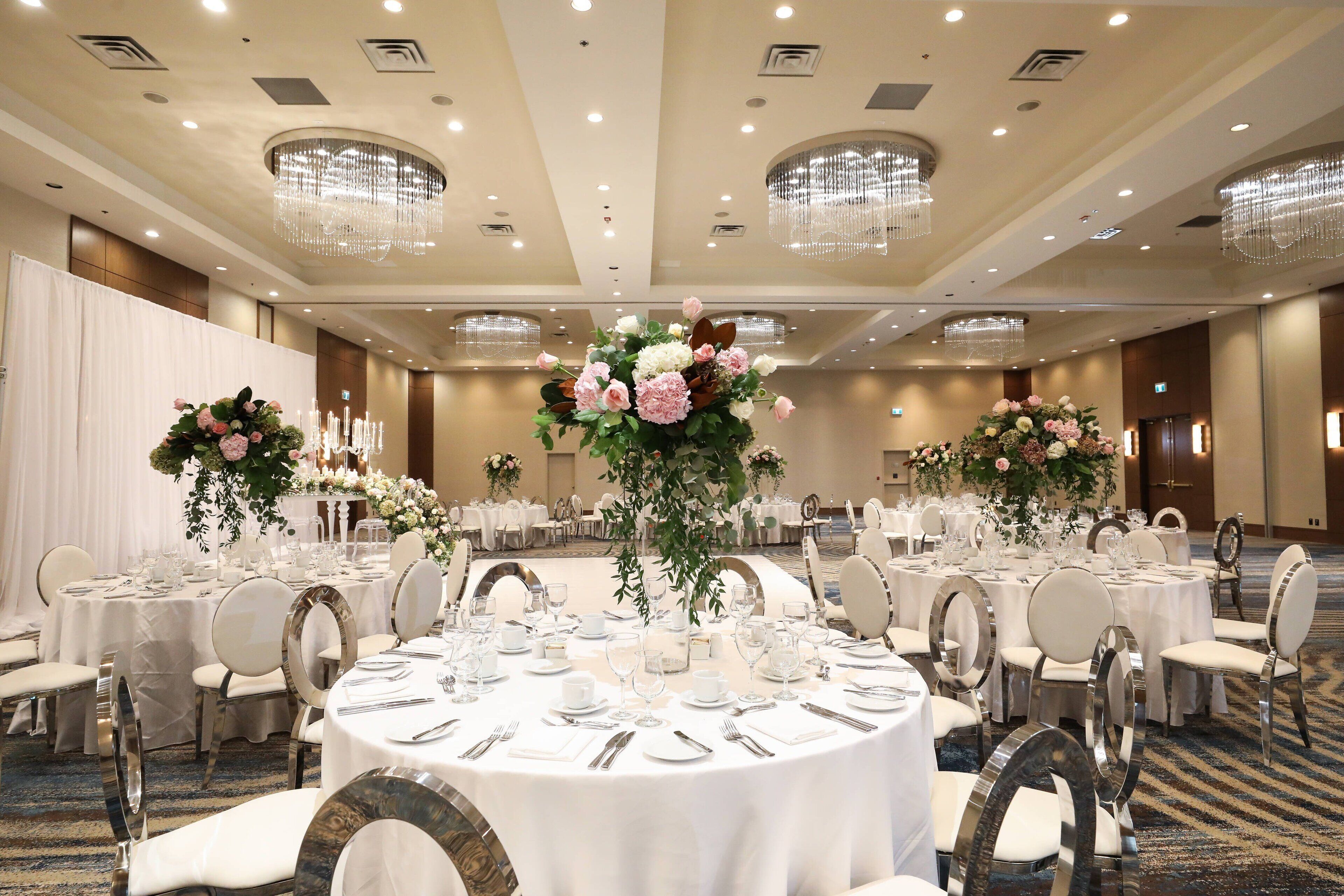 Ein Festsaal mit runden Tischen, weißen Tischdecken und floralen Mittelstücken.