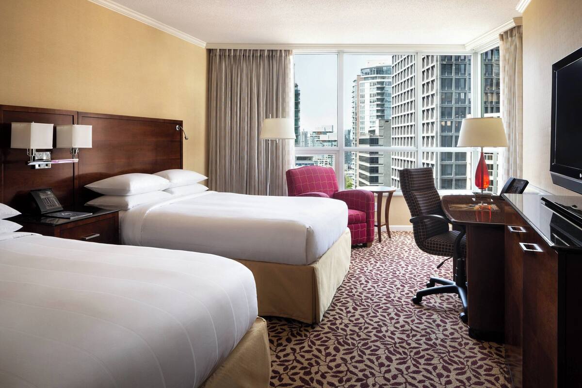 A hotel room with two beds, a desk with a computer, a chair, and a TV.