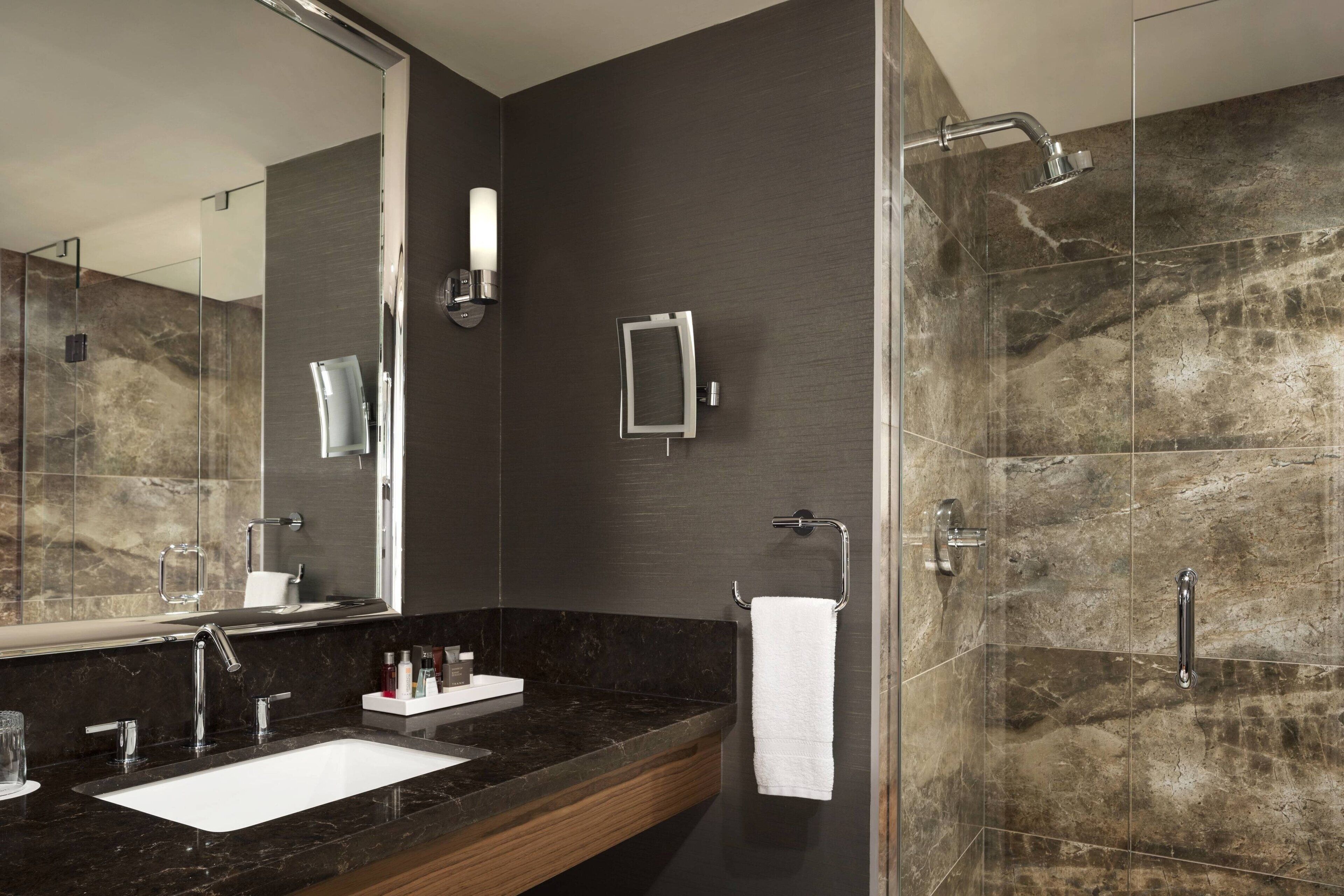 Un baño moderno con un espejo grande, un lavamanos, una ducha y un perchero para toallas.