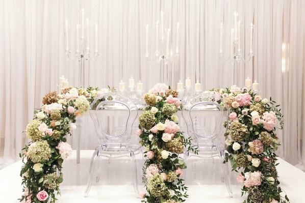 Una mesa dispuesta para un evento formal, con sillas elegantes, centros de mesa florales y velas.