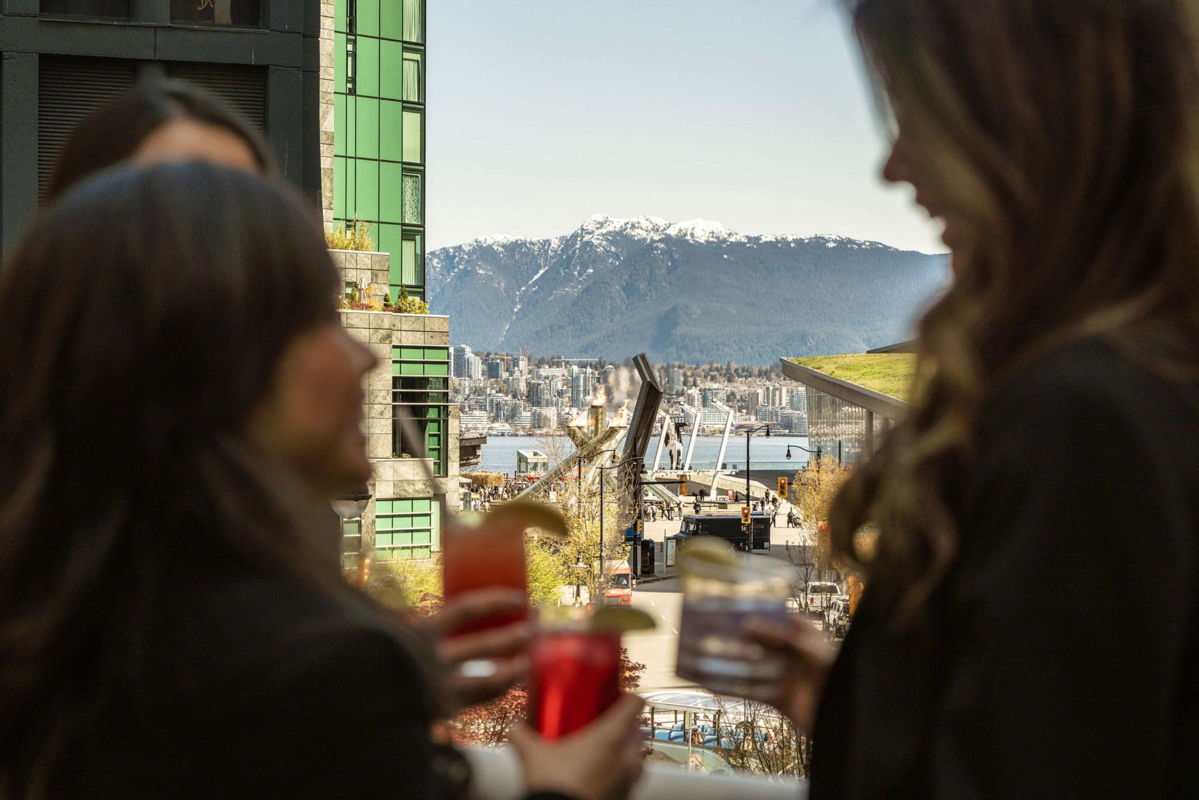 Two people holding drinks with a cityscape and mountains in the background.