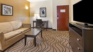 Une chambre d’hôtel avec un canapé, une petite table, un téléviseur, un bureau avec une chaise et une moquette à motifs.