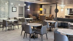 Un hall d’hôtel moderne avec des tables et des chaises rondes, un coin salon avec des canapés et un grand miroir.