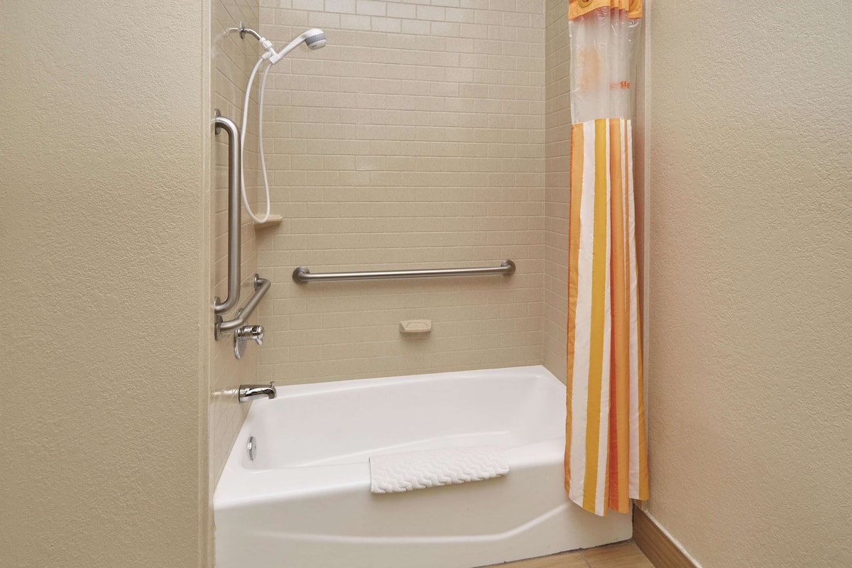 Een badkamer met een witte badkuip, een douche met een handdouche, een handgreep en een gestreept douchegordijn.