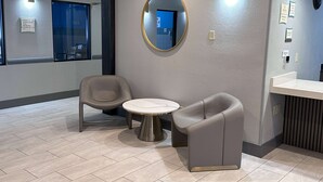 Un espace d’attente moderne avec une table ronde et deux chaises, un grand miroir au mur et un comptoir d’accueil.