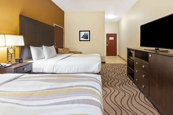 Une chambre d’hôtel avec deux lits, une télévision, une commode et une lampe.