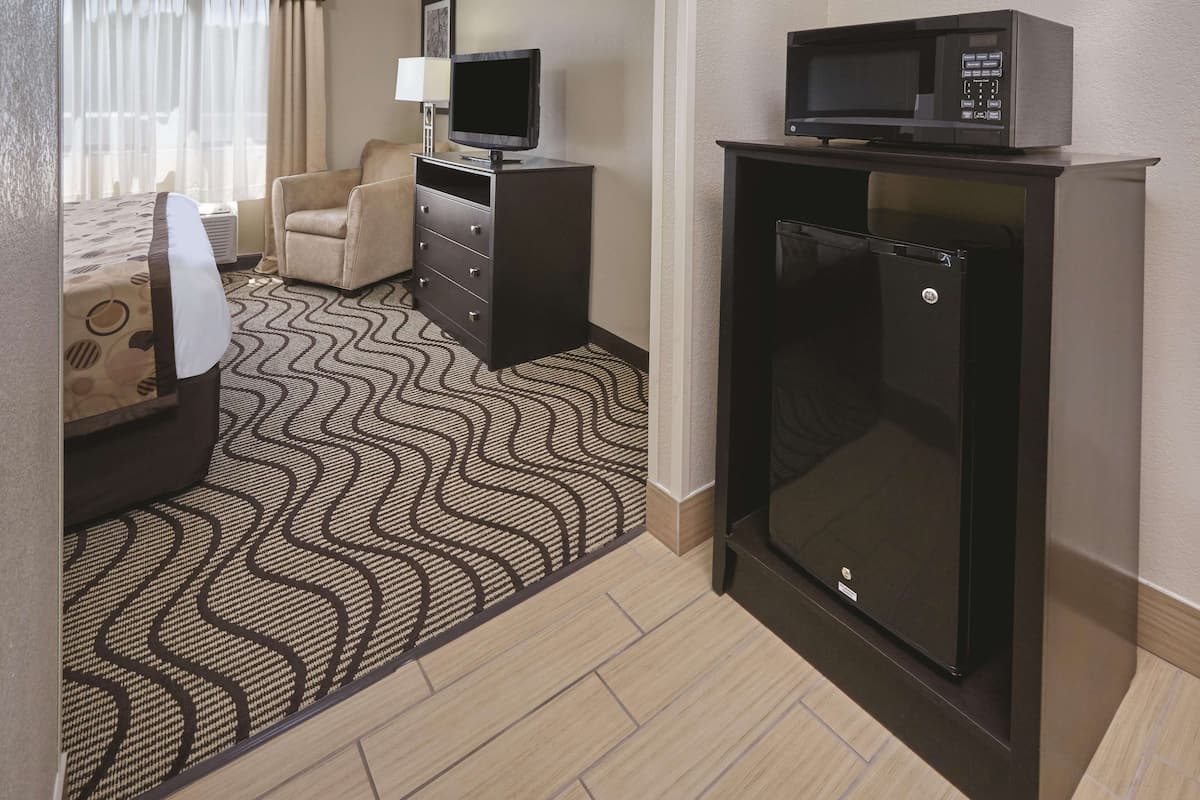 Een hotelkamer met een bed, een bureau met een computer, een stoel, een magnetron en een koelkast.