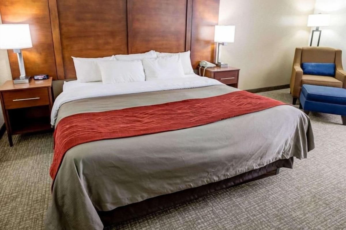 A hotel room with a large bed, two bedside tables, a chair, and a lamp.