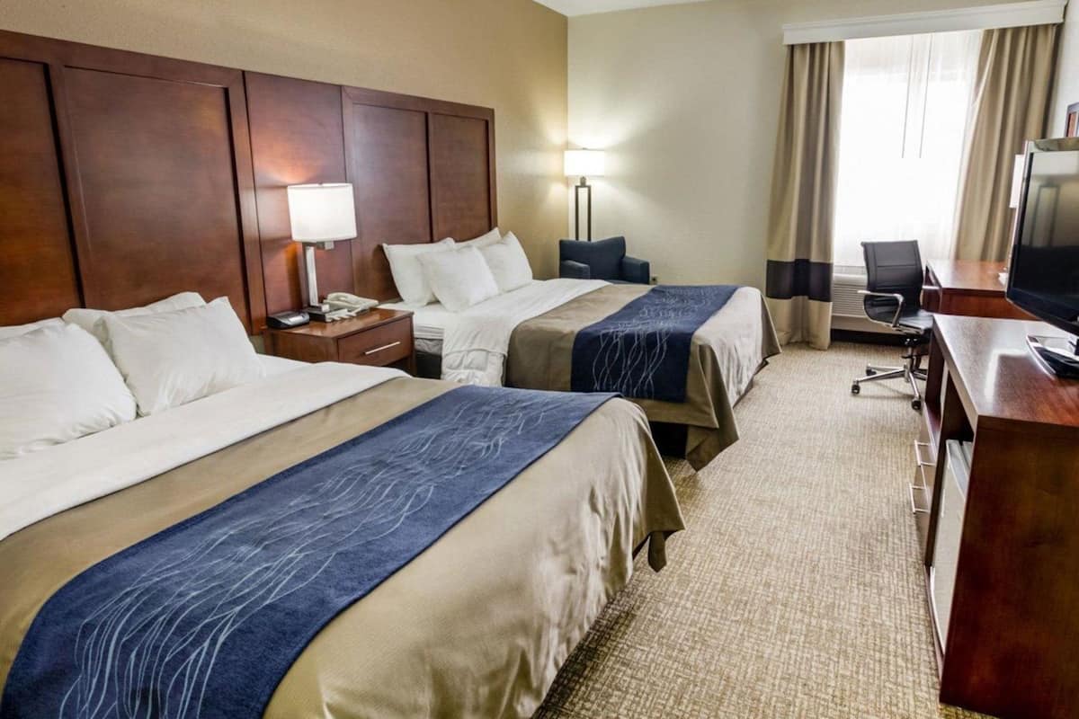 A hotel room with two beds, a desk with a computer, a TV, and a window with curtains.