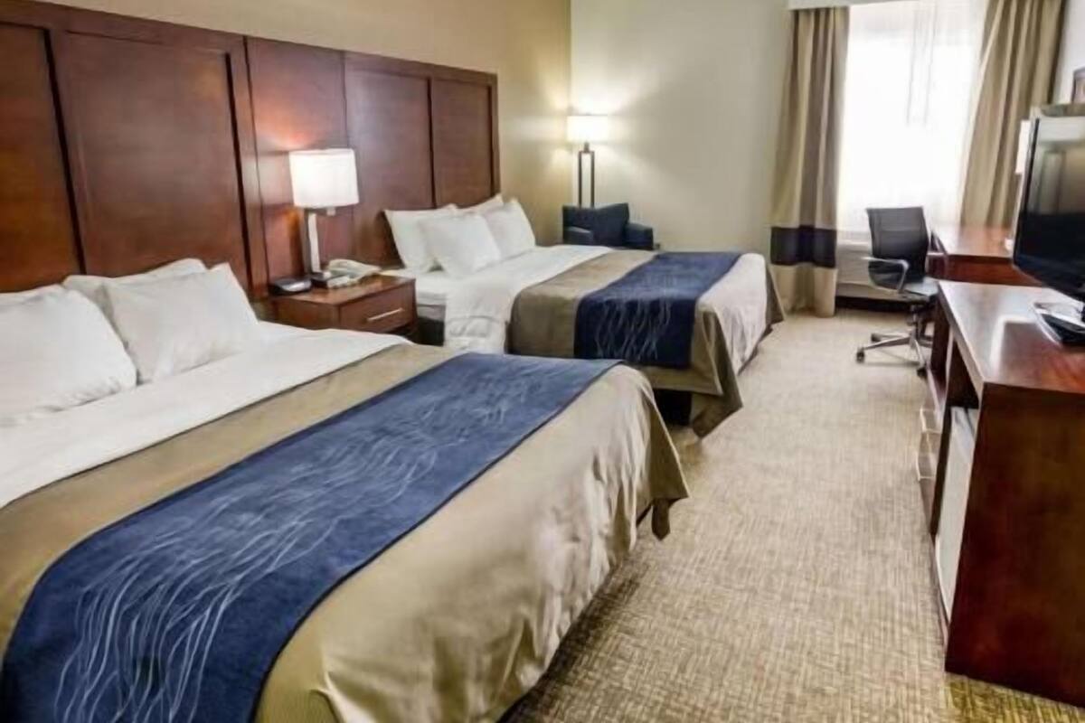 A hotel room with two beds, a desk, a chair, a TV, and a window with curtains.