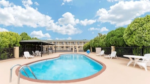 A swimming pool with lounge chairs and a covered seating area, surrounded by trees and a building in the background. - Days Inn by Wyndham Snyder (Snyder)