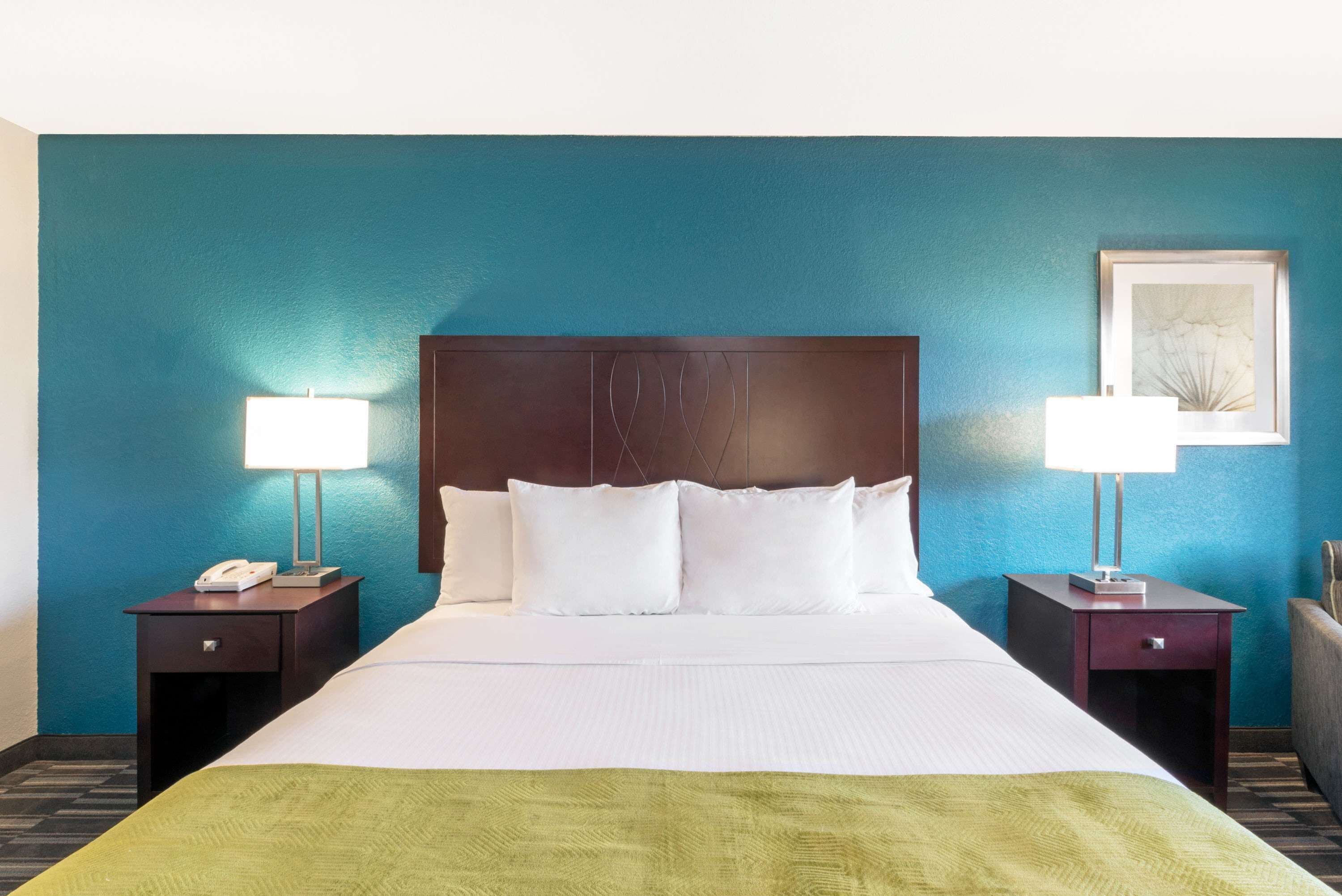 A hotel room with a large bed, two bedside tables with lamps, a framed picture on the wall, and a green throw blanket.