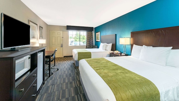 A hotel room with two beds, a desk with a television, a window with curtains, and a lamp. - Days Inn by Wyndham Snyder (Snyder)
