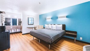 A modern hotel room with a bed, a small desk, a chair, and a kitchenette. - Americas Best Value Inn Beeville (Beeville)