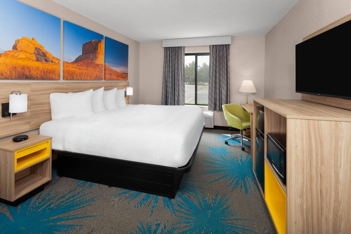 Habitación de hotel con una cama grande, un escritorio con televisor de pantalla plana, una silla y un ventanal con cortinas.