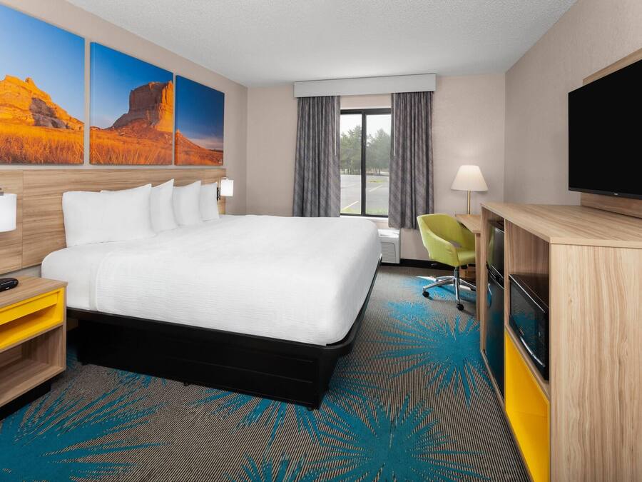 A hotel room with a large bed, a desk with a flat-screen TV, a chair, and a window with curtains.