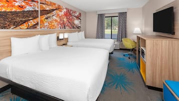 A hotel room with two beds, a TV, a desk, and a window with a view.