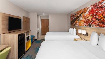 A hotel room with two beds, a TV, a desk with a microwave, and a painting of autumn leaves.