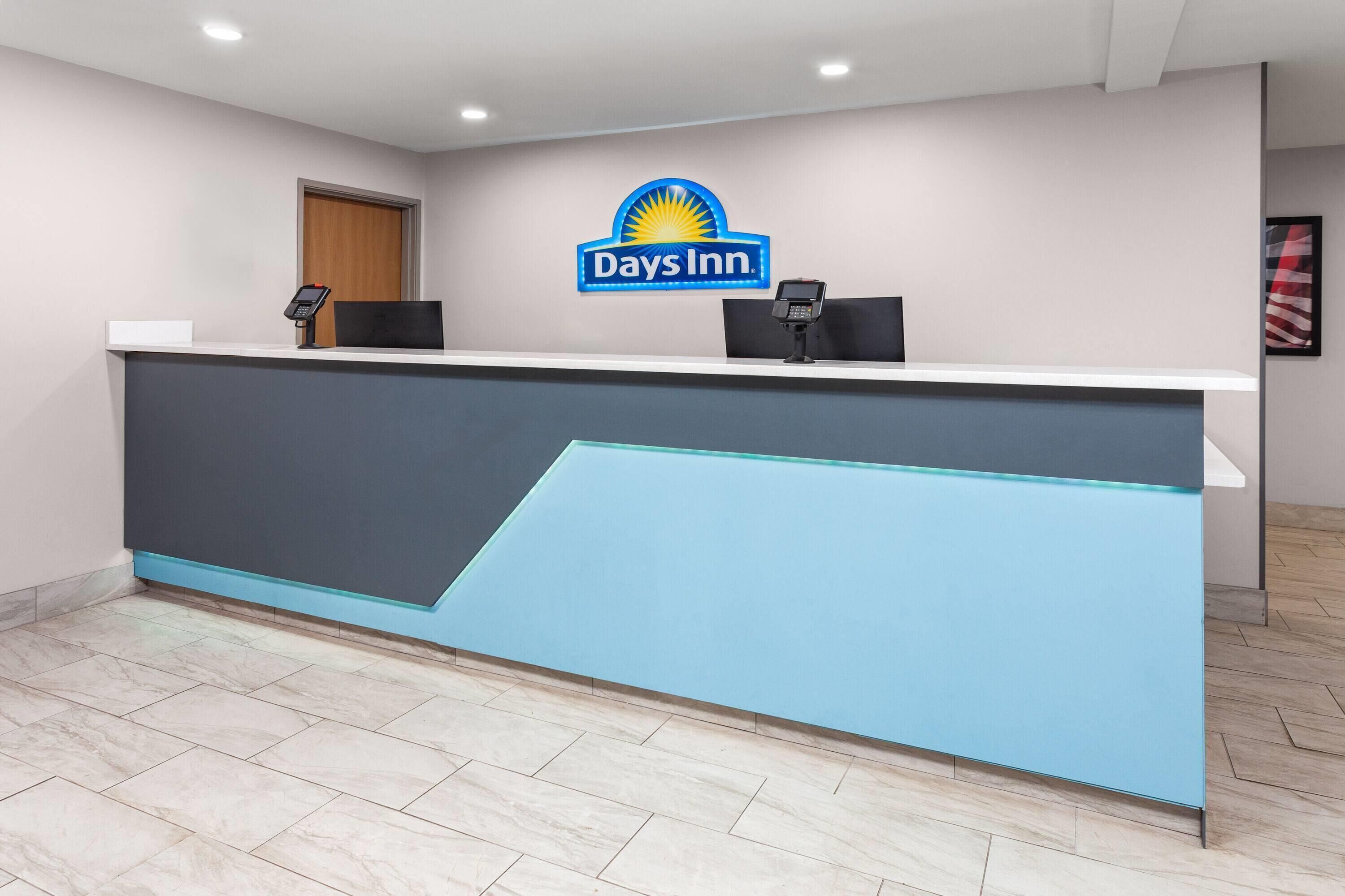 Un mostrador de recepción con el logotipo de Days Inn, dos teléfonos negros y una puerta de madera.