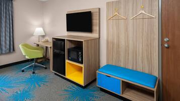 A hotel room with a desk, chair, television, wardrobe, and a bench.