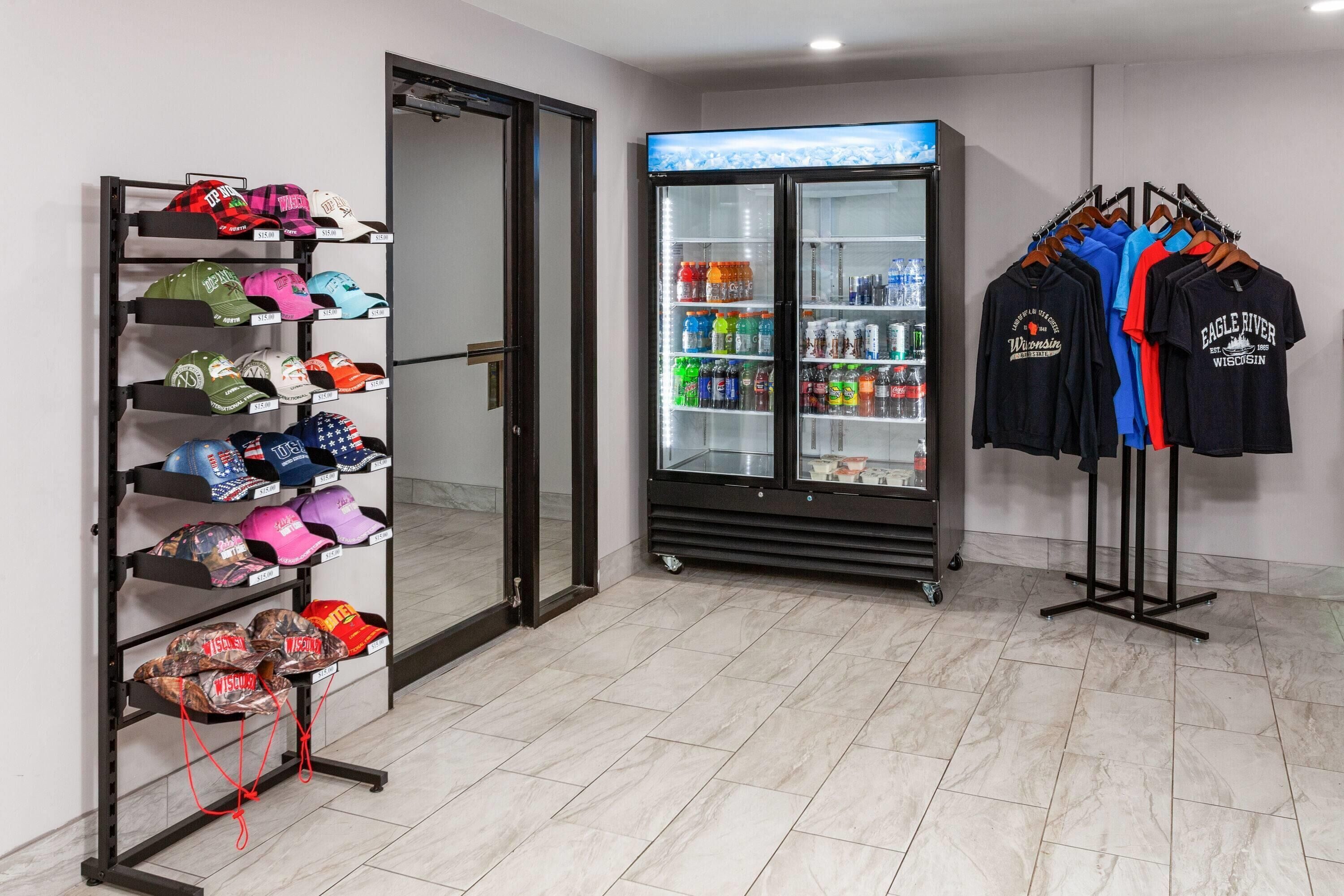 A retail space with a display rack of hats, a beverage refrigerator, and a rack of t-shirts.