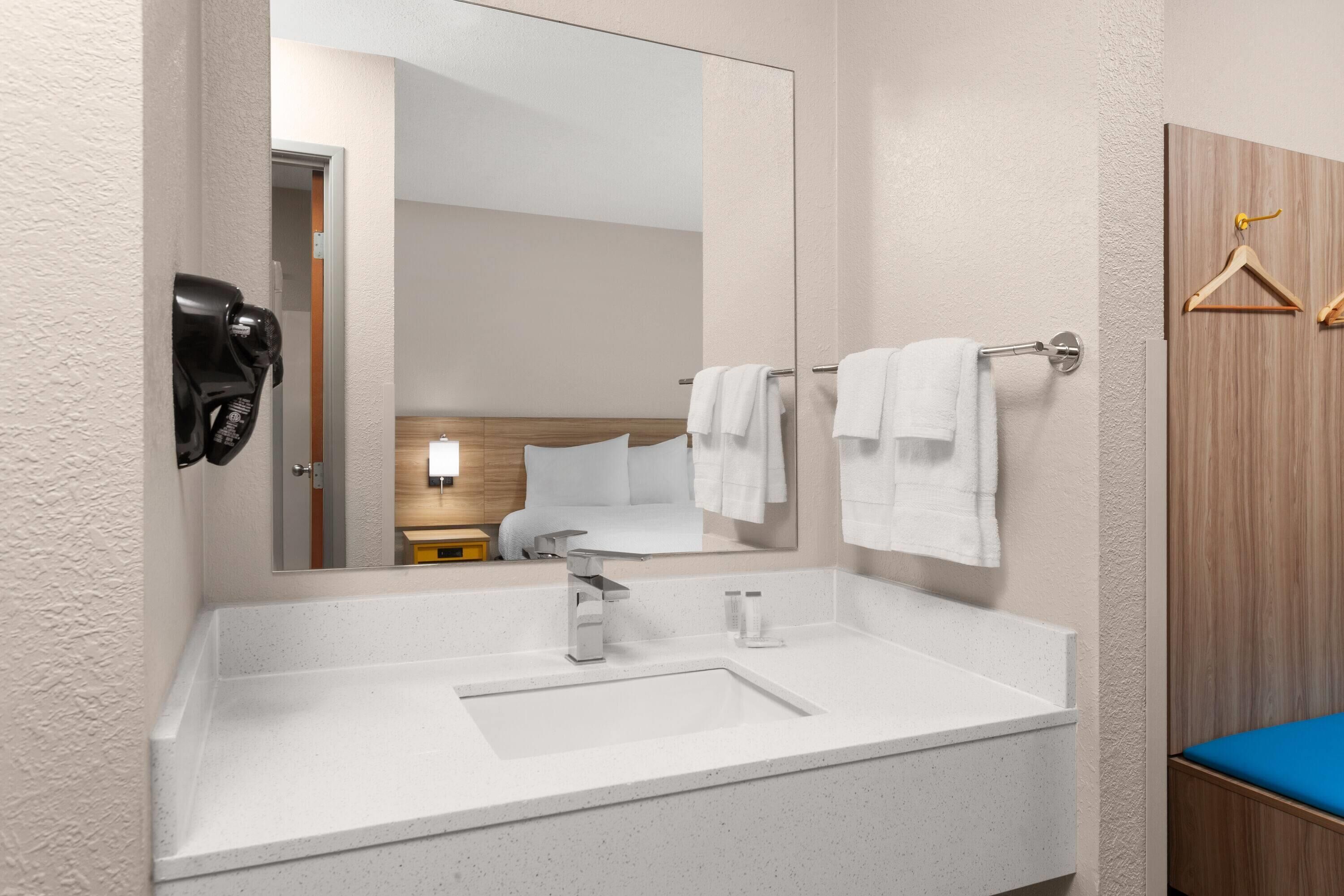 A modern bathroom with a large mirror, a white sink, and a towel rack.
