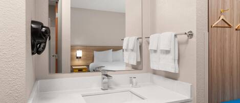 A modern bathroom with a large mirror, a white sink, and a towel rack.