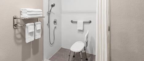 Un área de ducha con una silla blanca, un perchero con toallas dobladas y un cabezal de ducha.