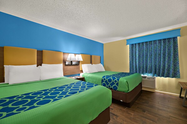 A hotel room with two beds, a nightstand, a lamp, and a window with curtains.